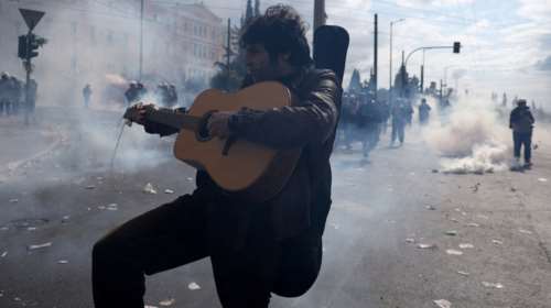 Τέμπη: Διαδηλωτής συνεχίζει να παίζει κιθάρα και φυσαρμόνικα εν μέσω των επεισοδίων στο Σύνταγμα - Απίστευτες εικόνες