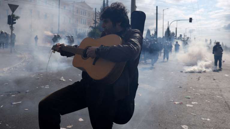 Τέμπη: Διαδηλωτής συνεχίζει να παίζει κιθάρα και φυσαρμόνικα εν μέσω των επεισοδίων στο Σύνταγμα - Απίστευτες εικόνες