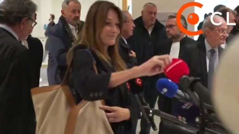 Κάρλα Μπρούνι: Το ειρωνικό χαμόγελο μετά την καταδίκη Σαρκοζί - &quot;Αρπάζει&quot; επιδεικτικά τηλεοπτικό μικρόφωνο [βίντεο]